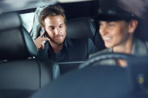 Businessman using cellphone in limousine, female chauffeur driving.